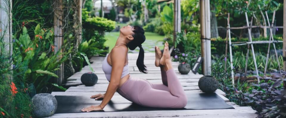 asyali kiz spor minderi uzerinde yoga yaparken yan goruntusu, saglikli yasam, bali adasindaki bahcede ahsap teras spor kiyafetleri giyen kadin