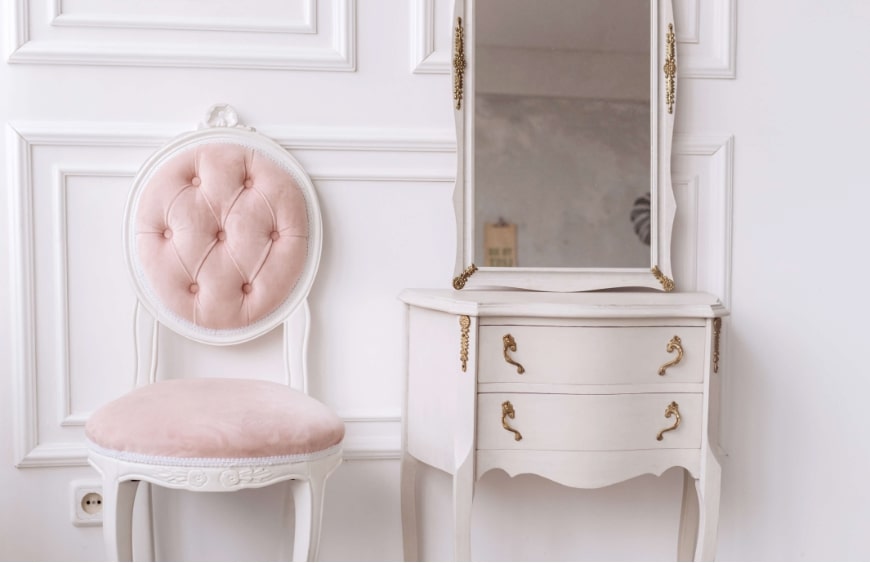 cita dekorlu klasik beyaz banyoda pudra pembe renk kaplama klasik sandalye ve altin varakli kulplari ile aynali etajer