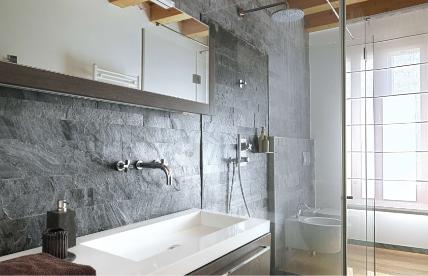dogal tas gorunumlu duvar karosu, ahsap kirisler, kahrevengi mobilyalari, buyuk lavabo tezgahi ile modern banyo