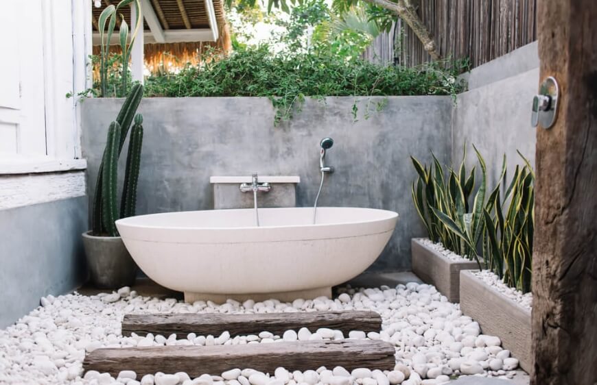 balide luks villa terasinda yerde cakil taslari, egzotik bitkiler ile dekore edilmis oval seramik kuvet ile modern acikhava banyosu