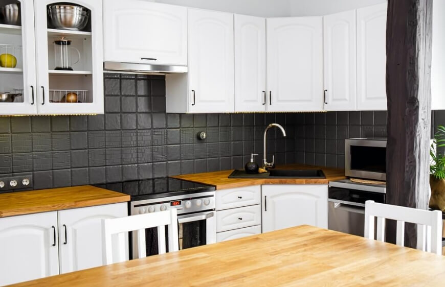 beyaz mutfak dolaplari, ahsap tezgah, siyah kare tezgah arasi ve mutfak kosesinde siyah eviye